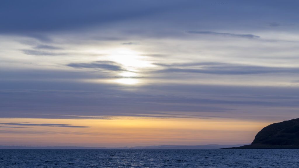 a grey and orange sunset over an empty anchorage with an island on the right hand side