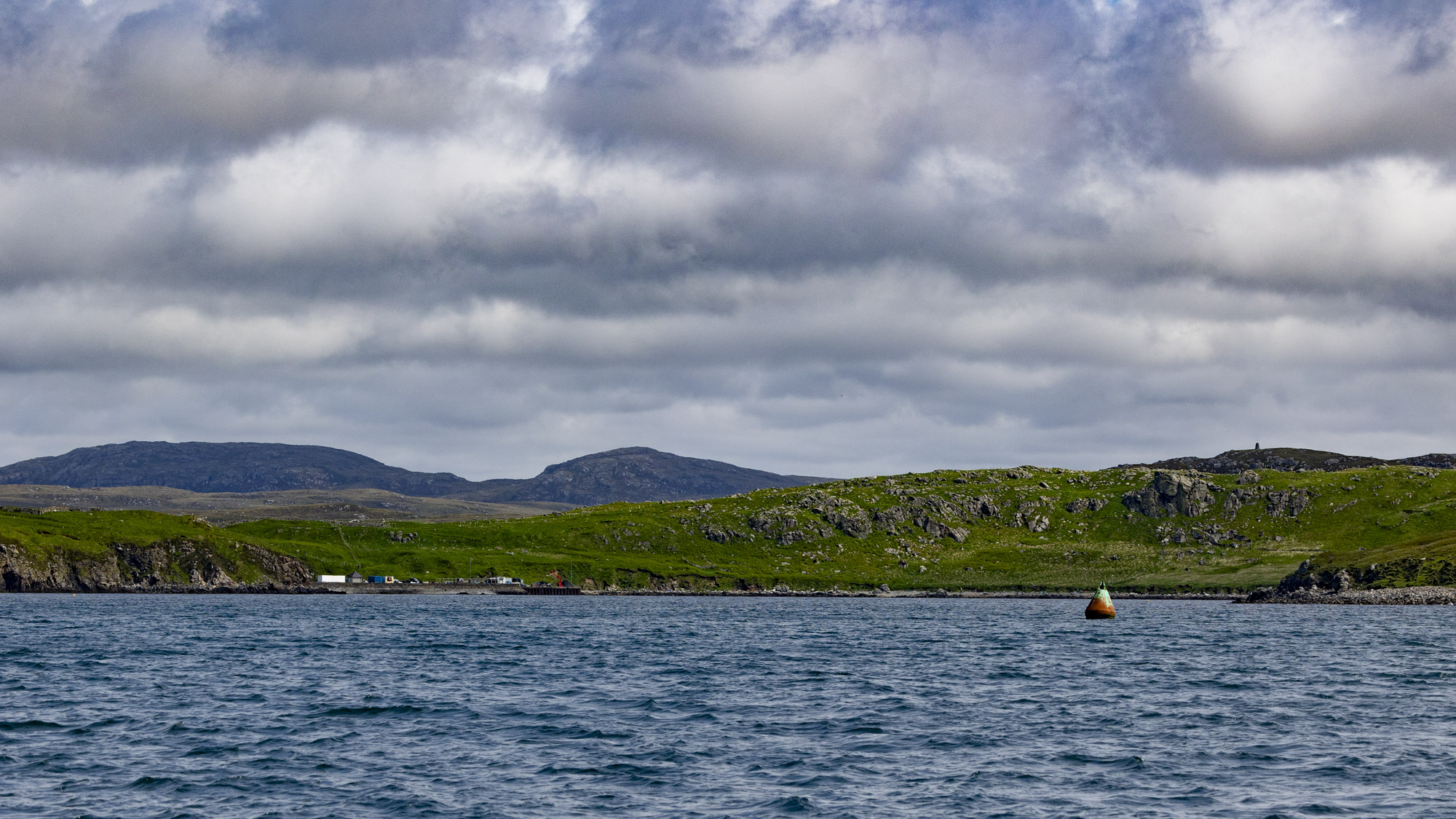 Low rocky hills over a seascape with a green buoy in the foreground