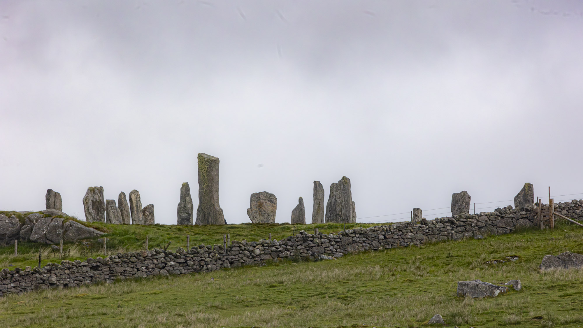 A complex of megaliths stand against a threatening sky on in a wet green field