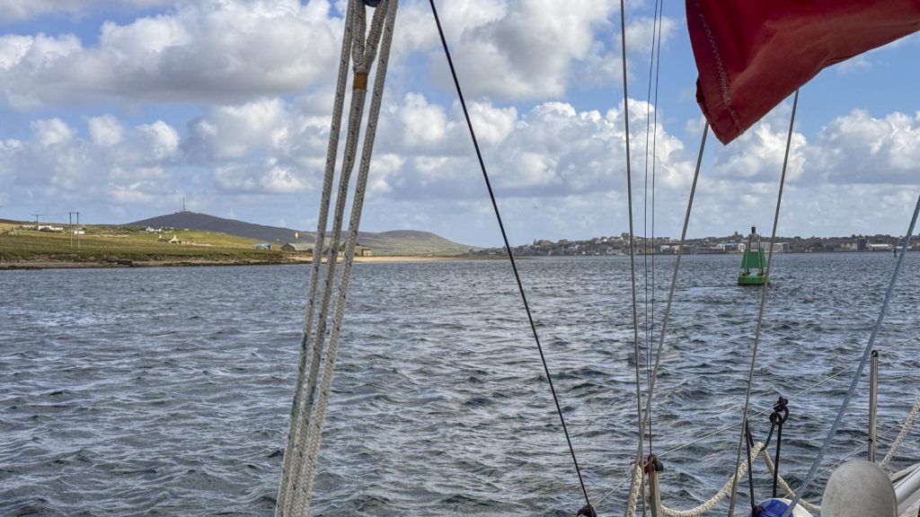 In the calm waters of Lerwick Harbour, with the green island of Bresay on the left, and the riggin of Trilleen in the foreground