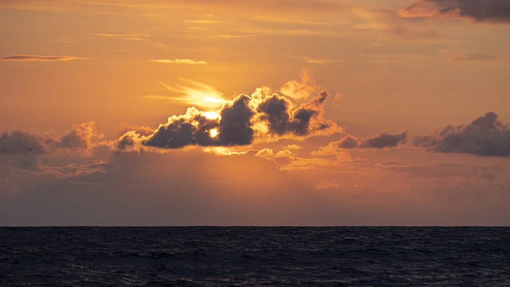 Nightfall south of Fairisle, the vast orb of the sun partly occluded by light cumulus over a darkening sea