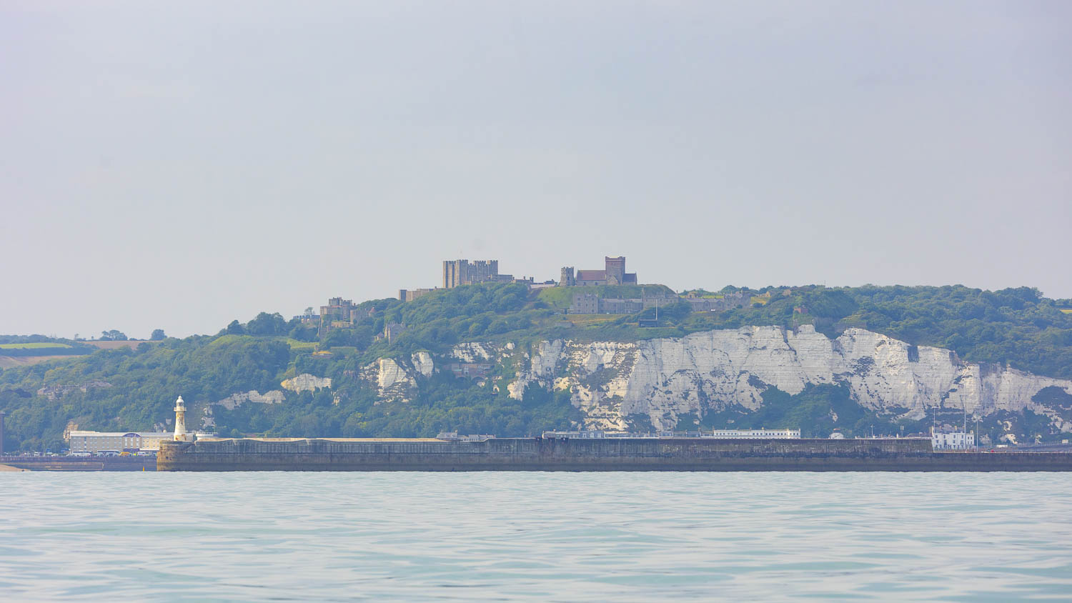 A honey yellow castle rises from sheer white cliffs with a breakwater pa their foot